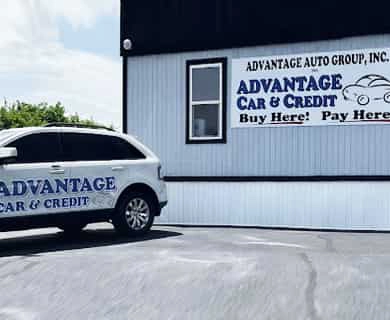 White SUV with Advantage Car & Credit branding parked in front of a light-colored building with a sign that says ‘Advantage Car & Credit’ and ‘Buy Here Pay Here’.