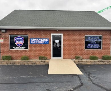 Brick storefront auto loan office with blue signage on either side of a central door, a concrete ramp to the entrance, and low shrubs along the front.