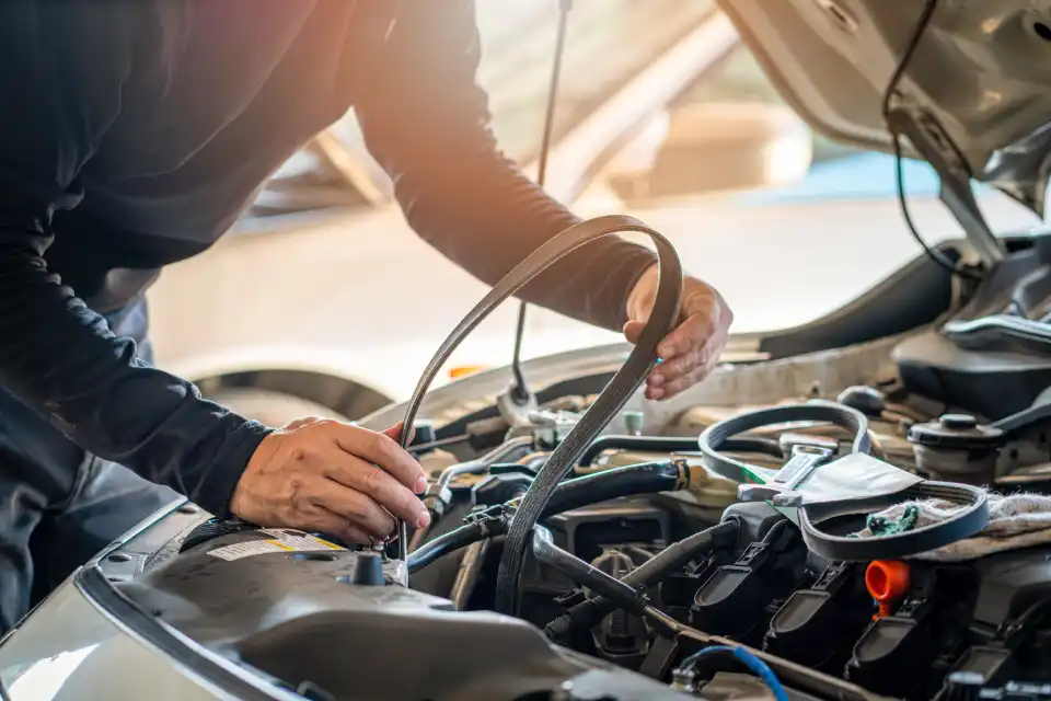 Mechanic inspecting a car engine and guiding a hose under the open hood.